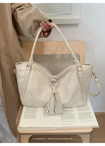 Close-up of cream PU leather tote bag featuring woven edges and decorative tassel details