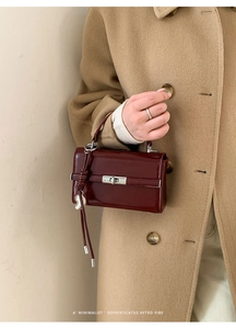 Detail of dark red patent leather handbag with silver twist lock and tassel charm