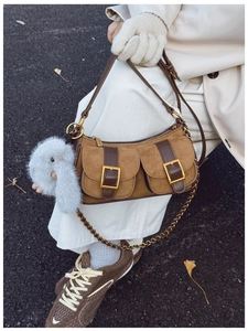 Detail of a brown suede hobo bag with gold buckles and a grey fluffy rabbit charm