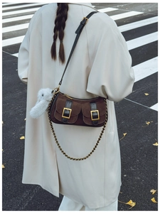 Detail view of brown suede dumpling bag with double gold buckle pockets and plush rabbit charm