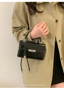 Detail view of a black glossy leather retro handbag with silver metal twist lock and pendant