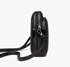 Detail view of black lychee grain leather crossbody bag with triple silver zipper compartments