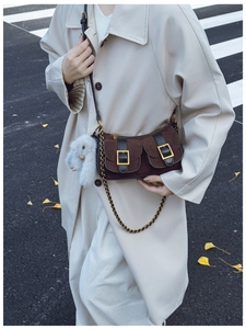 Detail of dark brown suede crossbody bag with metal buckles and a cute plush rabbit charm