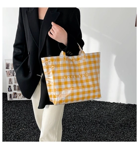 Detail view of yellow plaid tote bag with TOTE BAG print held by a fashion model