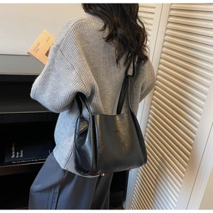 Detail shot of the black bucket bag showing polished leather texture and gold metal feet