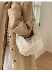 Detail of minimalist cream canvas dumpling bag with dual zipper pockets and decorative straps