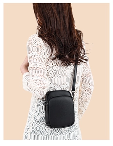 Detail of mini black lychee leather crossbody bag on white lace outfit with metal zippers