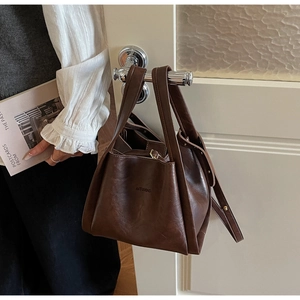 Detail of a dark brown leather tote bag featuring golden hardware and embossed brand text