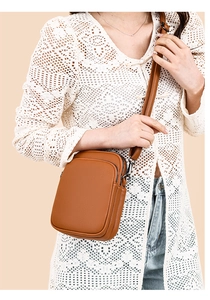 Close-up of brown leather mini crossbody bag with multi-layer zipper and silver hooks