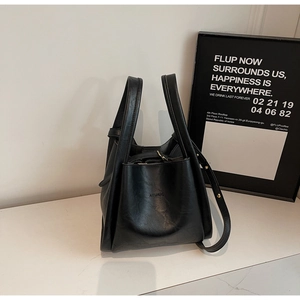 Minimalist black leather bucket bag with top handles and gold-studded shoulder strap