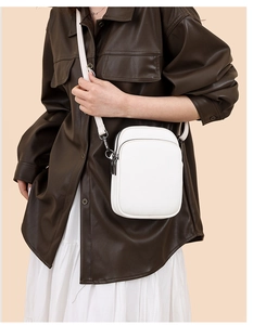 Detail view of white pebbled leather crossbody bag with three zipper compartments and strap
