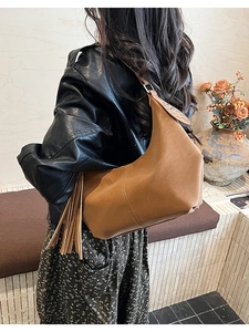 Brown leather crescent bag with decorative tassels and metallic ring shoulder strap