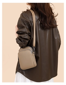 Detail of khaki leather mini crossbody bag with three zipper compartments worn by model