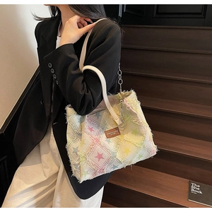 Close-up of denim tote bag with colorful stars, frayed edges and leather brand label