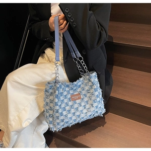 Detail of blue and white checkered denim tote bag with leather label and chain strap