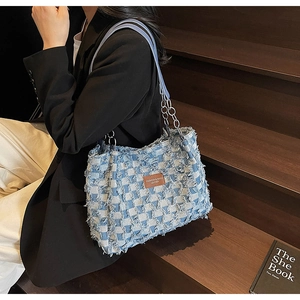 Close-up of blue plaid denim tote bag featuring fringed edges and metal chain strap
