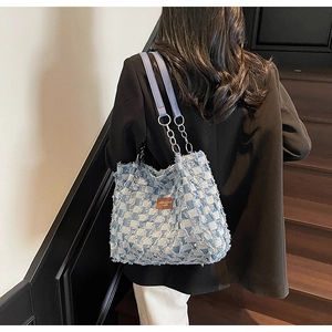 Detail of blue and white checkered denim tote bag with frayed edges and brown leather patch