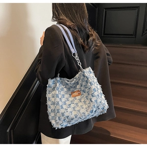 Detail view of denim checkerboard tote bag with distressed frayed edges and chain strap