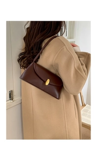 Brown leather baguette bag with gold buckle worn on shoulder by model in modern setting