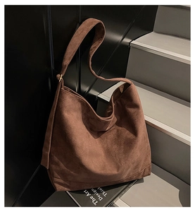 Detailed close-up of a large brown suede tote bag with wide shoulder strap on stairs