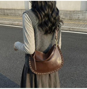 Detail view of deep brown crescent bag with gold cylindrical studs and matte leather finish