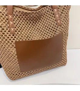 Close-up of beige woven straw tote bag featuring a brown leather pocket and cross-stitched straps