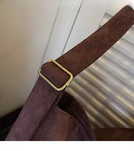 Detail of a brown faux suede tote bag featuring a gold metal buckle and wide strap