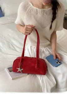 Detail of a red suede baguette bag with long handles and a silver starfish pendant