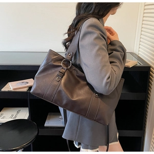 Detail of dark brown leather tote bag with metal rings and reinforced rivets on shoulder strap