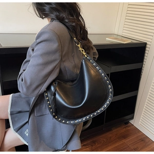 Detail view of black leather hobo bag featuring gold studs and slim shoulder strap on model