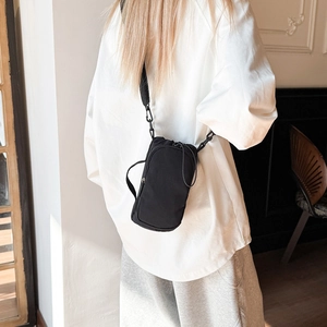 Detailed close-up of a black minimalist nylon crossbody bag worn by a model in a home setting