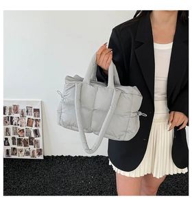 Close-up of light gray quilted puffer tote bag with padded texture and side drawstrings