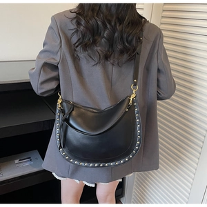 Detail of black leather half-moon bag with metallic studs on a model in a grey blazer