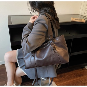 Detail of a large vintage brown soft leather tote bag worn by a model in a home setting