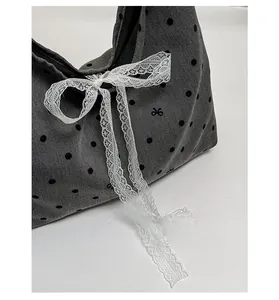 Detail of grey polka dot canvas tote featuring a white lace ribbon and bow embroidery