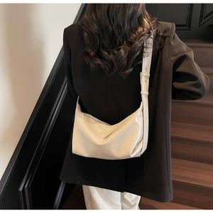 Detailed back view of a cream half-moon crossbody bag worn by a model on stairs