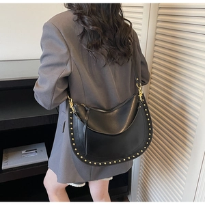 Close-up of black crescent saddle bag with gold rivets and metallic rotating buckle