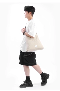 Dettaglio della borsa a tracolla beige con etichetta logo decorativa e trama in nylon