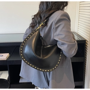 Detail of black leather crescent bag with golden studs and metal hooks worn by model