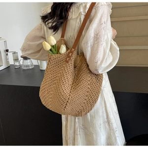 Detail of woven straw tote bag featuring brown leather shoulder straps and reinforced stitching