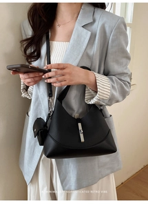 Detail of black leather Hobo bag with silver metal buckle and mini charm on strap