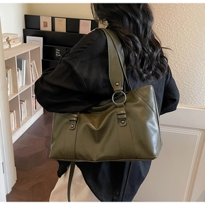 Detailed view of dark olive leather tote bag with wide strap and metal hardware