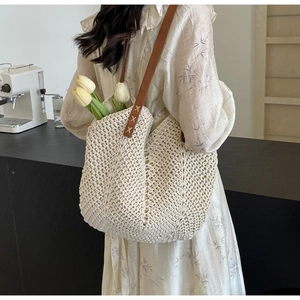 Close-up of beige crochet tote bag with brown leather strap and intricate knit patterns