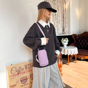 Detail of a small light purple nylon crossbody bag with adjustable strap and zipper closure