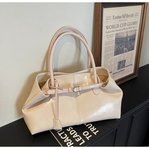 Détail d'un sac cabas crème brillant avec sangle à boucle décorative et pendentif latéral