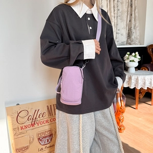 Close-up of a purple canvas crossbody phone bag with an adjustable strap in a cafe