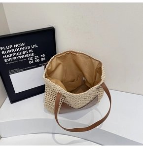 Detail view of woven straw tote bag featuring brown leather straps and fabric lining