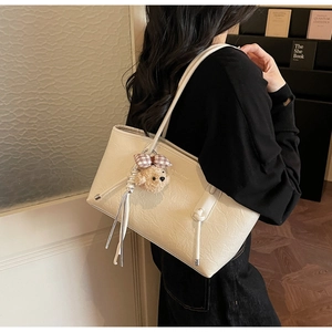 Dettaglio di una borsa tote beige con trama a pieghe e un simpatico ciondolo a orsetto