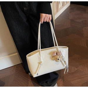 Dettaglio della borsa tote off-white con trama, decoro a nodo e ciondolo a orsetto