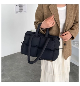 Detail of black quilted puffer tote bag with glossy nylon texture and soft padded handles